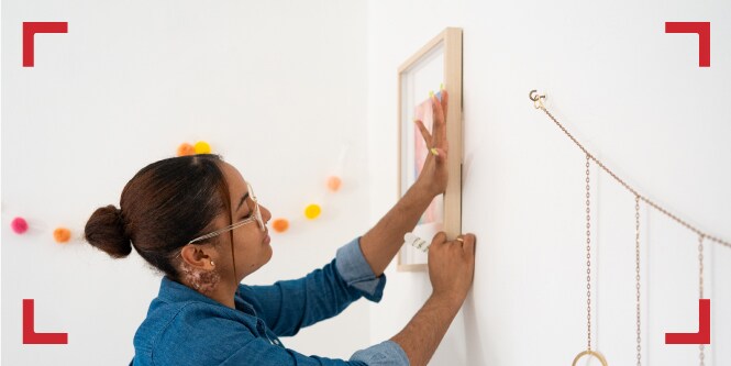 Mujer decorando sin herramientas, con tiras adhesivas para cuadros Command.
