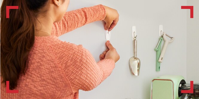 Mujer organizando sin herramientas, colgando accesorios de cocina con ganchos Command.

